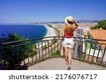 Back view of beautiful young woman holding hat enjoying view of the cityscape of Nice, France