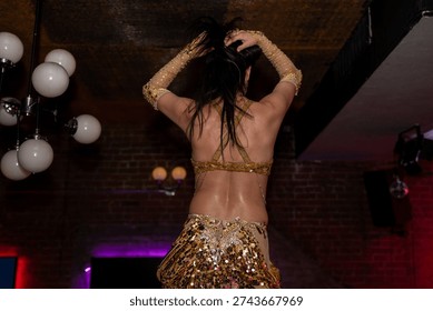 Back view of belly dancer performing on stage.