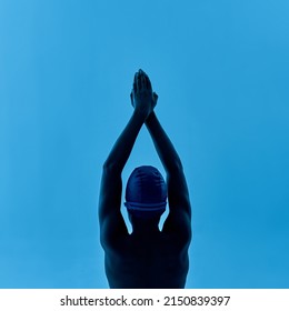 Back View Of Black Boy Swimmer In Swim Pose. Cropped Image Of Male Youngster Wearing Swimming Cap And Goggles. Modern Child Sportive Lifestyle. Isolated On Blue Background. Studio Shoot. Copy Space