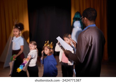 Back view of Black drama teacher directing school play with group of children on stage in theater copy space - Powered by Shutterstock