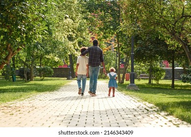 Back View Of Black Family Walk On Pavement Road In Green Park. Father Hugging Son And Holding Hand Of Little Daughter. Family Relationship And Spend Time Together. Fatherhood And Parenting. Sunny Day