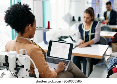 Back View Of Black Fashion Designer Using Laptop And Analyzing New Clothing Designs At Sewing Factory. 