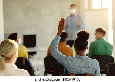 Back view of black female student raising arm to ask a question during a lecture in the classroom. 