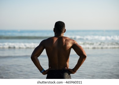 Back View Of Black Fit Sportsman Looking The Sea For Motivation Before Swimming. Male Swimmer Ready For Outdoor Training Into The Ocean.