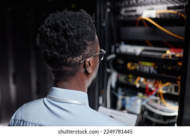 Back view of black man as network engineer working with server cabinet in data center, copy space