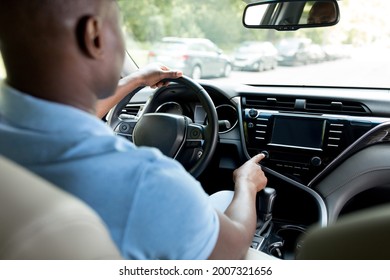 Back View Of Black Man Sitting At New Car Front Seat, Making Test Drive, Turning Music On, Checking Automobile Stereo System, Closeup, Copy Space. Unrecognizable African American Driver Going To Job