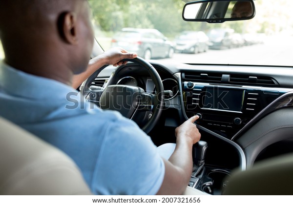 Back view of black man sitting at new car front seat,\
making test drive, turning music on, checking automobile stereo\
system, closeup, copy space. Unrecognizable african american driver\
going to job