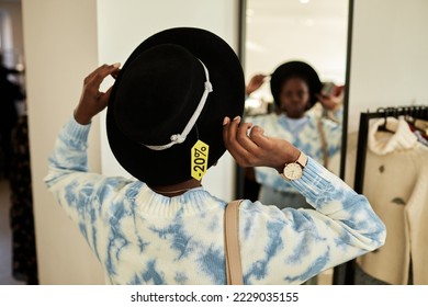 Back view of black young woman trying on hat in thrift store and looking in mirror, focus on sale tag, copy space - Powered by Shutterstock