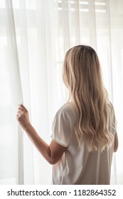 Back View Of A Blond Hair Woman Looking Outside The Window