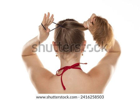 Back view of blond women that tightens the hair in a ponytail on white studio background