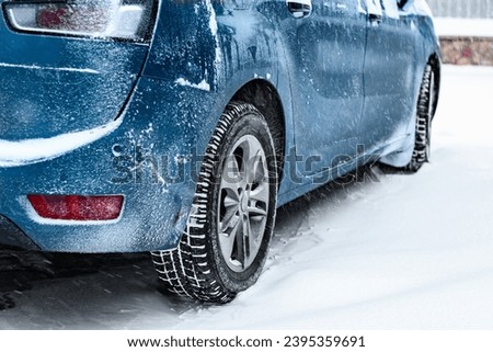 Back view of blue car covered with snow parked on snow covered road.