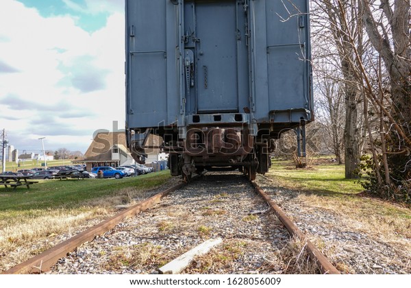 Back view of a blue railroad\
car on tracks. The car coupler mechanism and undercarriage are\
rusted