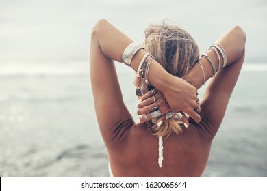 Back view of boho styled and tanned girl wearing ethnic indian silver jewelry looking at horizon on the beach in Bali