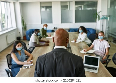 Back View Of Boss Tell To Blurred Employees At Corporate Meeting In Office. Multiracial People Wear Medical Masks. Business Cooperation And Teamwork During Covid-19 Epidemic. Leadership And Management