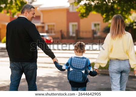 Back view of boy with backpack walking to school with parents, holding hands, first day back to school, family support