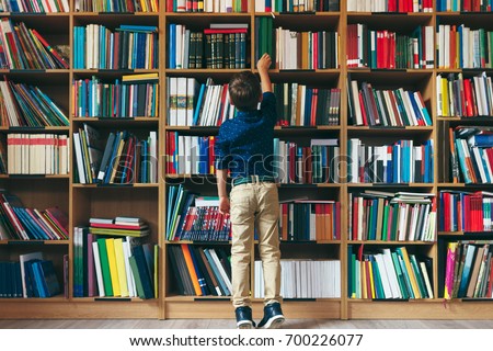Back view, boy stretches after a book on multi colored bookshelf in library. Education, Knowledge, Bookstore, Lecture.