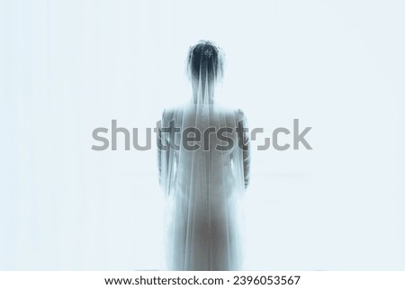 BACK VIEW OF BRIDE STANDING AGAINST WHITE BRIGHT WINDOW BACKGROUND HIGH KEY 