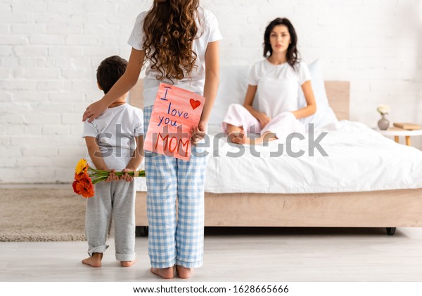 back view of brother and sister holding flowers and i love you mom card