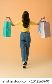 Back View Of Brunette Woman In Jeans Holding Shopping Bags On Orange Background