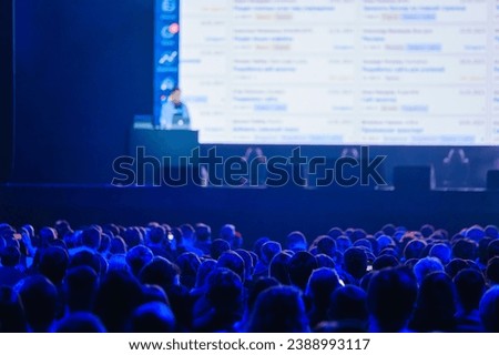Back view of business crowd attending global presentation in illuminated blue auditorium