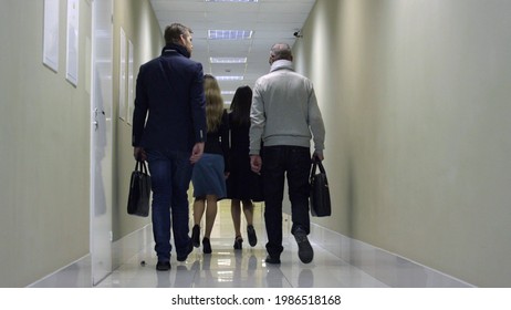 Back View Of Business Team Walking Down Corridor In Modern Office Building. Successful Business People Going To Board Meeting In Modern Business Center Hallway