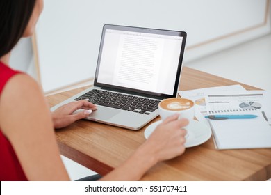 Back View Of Business Woman In Red Shirt Sitting On Workplace With Laptop, Cup Of Coffee And Documents