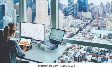 Back View Of Business Woman Sitting At Panoramic Skyscraper Office Desktop Front PC Computer With Financial Graphs And Statistics On Monitor.Analysis Of Digital Market And Investment In Block Chain