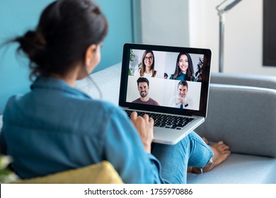 Back View Of Business Woman Speaking On Video Call With Diverse Colleagues On Online Briefing With Laptop On Sofa At Home.