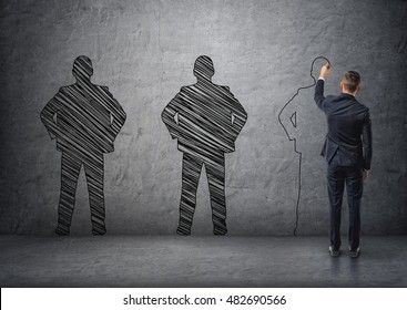 Back View Of A Businessman Drawing Dark Men's Silhouettes On Concrete Wall. Employment Issues. Outlines And Contours.