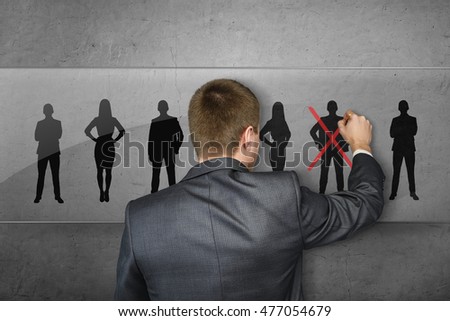 Back view of a businessman in front of a row of sihlouettes drawing red cross on one of the people. Dismissing, flunking, relieving. Big boss. Business staff.