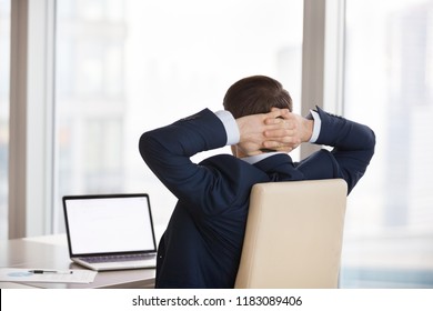 Back view of businessman sitting in office chair hands over heads working at laptop, male manager stretching looking at computer screen, man taking break distracted from job admiring view from window - Powered by Shutterstock