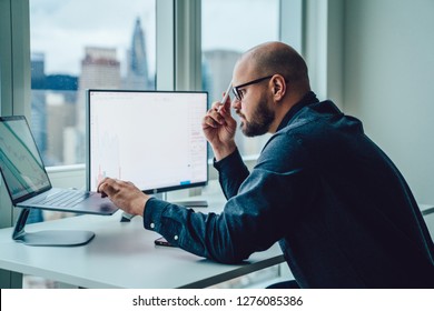 Back View Of Businessman Sitting At Office Desktop Front PC Laptop Computers With Financial Graphs And Statistics On Monitor.Making Research, Analysis Of Digital Market And Investment In Block Chain