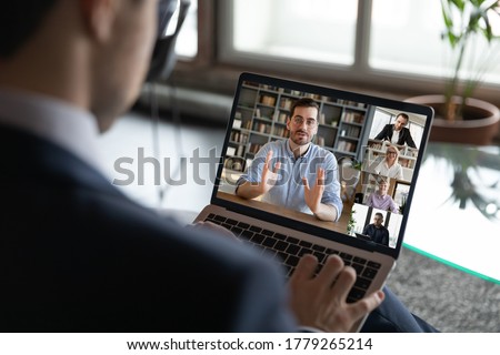 Back view of businessman talk on video call on laptop with multiracial employees or colleagues, male boss have webcam conference or virtual event with diverse businesspeople, use internet on computer