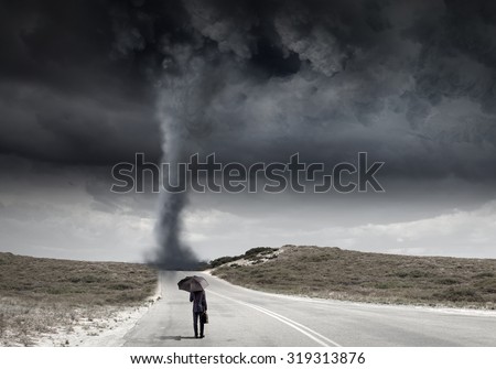 Back view of businessman with umbrella and suitcase facing tornado