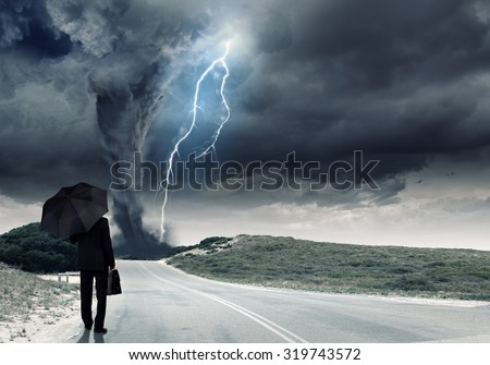 Back view of businessman with umbrella and suitcase facing tornado