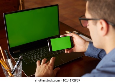 Back view of businessman using smartphone and laptop typing in office. Green screen mockup. Freelancer workspace. People and technology. Copyspace and product placement. - Powered by Shutterstock