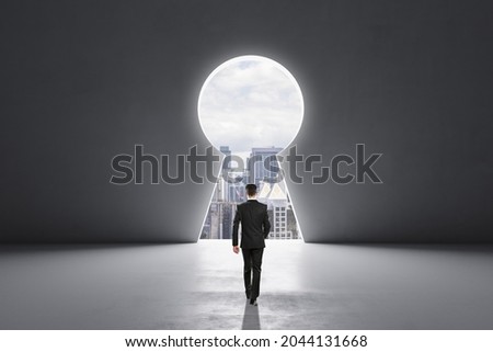 Back view of businessman walking in concrete interior with abstract keyhole window with city view. Key to success and career growth concept. Mock up place