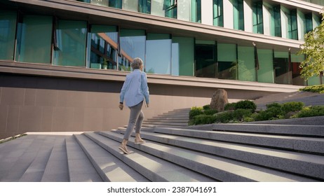 Back view businesswoman middle-aged lady manager CEO entrepreneur leader professional lawyer unrecognizable woman walking outdoors to office building city business center walk up stairs climbing steps - Powered by Shutterstock