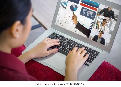 Back view of businesswoman in red dress typing on laptop computer keyboard while videoconference on-line meeting with the investment advisor. Work from home concept