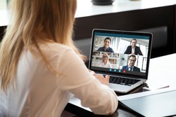 女商人在笔记本电脑上使用网络摄像头会议与不同的同事交谈，女员工与在家中进行在线简报的多种族同事进行视频通话的后视图