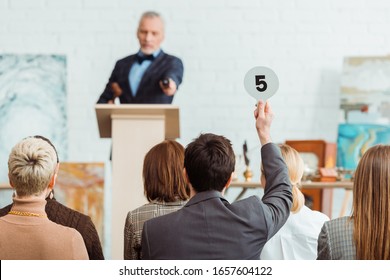 back view of buyer showing auction paddle with number five to auctioneer during auction - Shutterstock ID 1657604122
