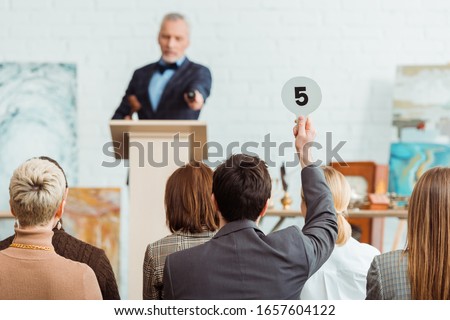 back view of buyer showing auction paddle with number five to auctioneer during auction Stockfoto © 