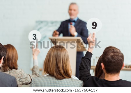 back view of buyers showing auction paddles with numbers nine and three to auctioneer during auction