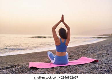 Back view of calm serene bliss satisfied fitness woman doing yoga meditation and breathing exercises on the beach by the sea. Mental mind care and healthy habits