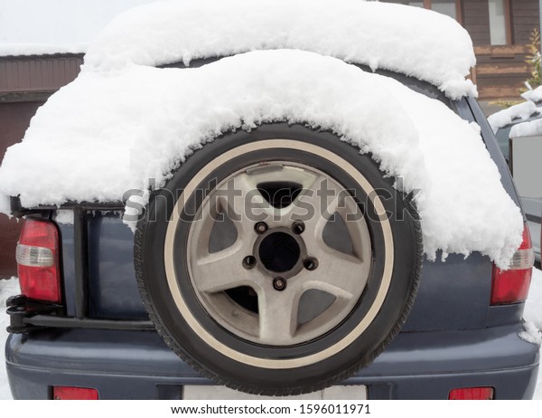 Back view of car with spare wheel.\
Off-road vehicle with stepney tire covered with\
snow
