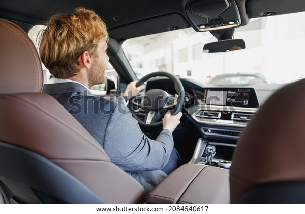 Back view caucasian businessman blond man driver\
male cabdriver wearing classic grey suit driving car holding wheel\
in traffic jam testing auto want buy new automobile vehicle Sale\
transport concept