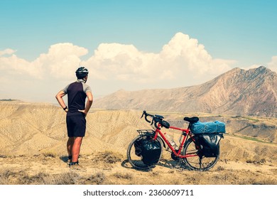 Back view caucasian male cyclist standing by red touring bicycle looking to scenic mountains background. Active inspirational lifestyle concept
