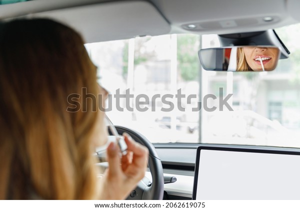 Back view caucasian woman drive hold put hand on\
steering wheel look at mirror paint lips with lipstick sitting in\
auto new car automobile in traffic jams Female driver feminine lady\
lifestyle concept