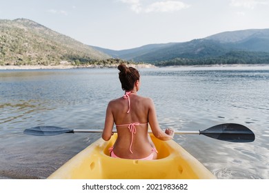 Back View Of Caucasian Woman In Swim Wear Holding Oar Sitting On Yellow Canoe In Lake During Sunny Day. Woman Ready To Row. Summer Time. Sports, Adventure And Nature