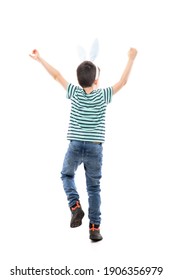 Back view of cheerful excited young boy with Easter bunny ears celebrating with raised hands. Full length isolated on white background.